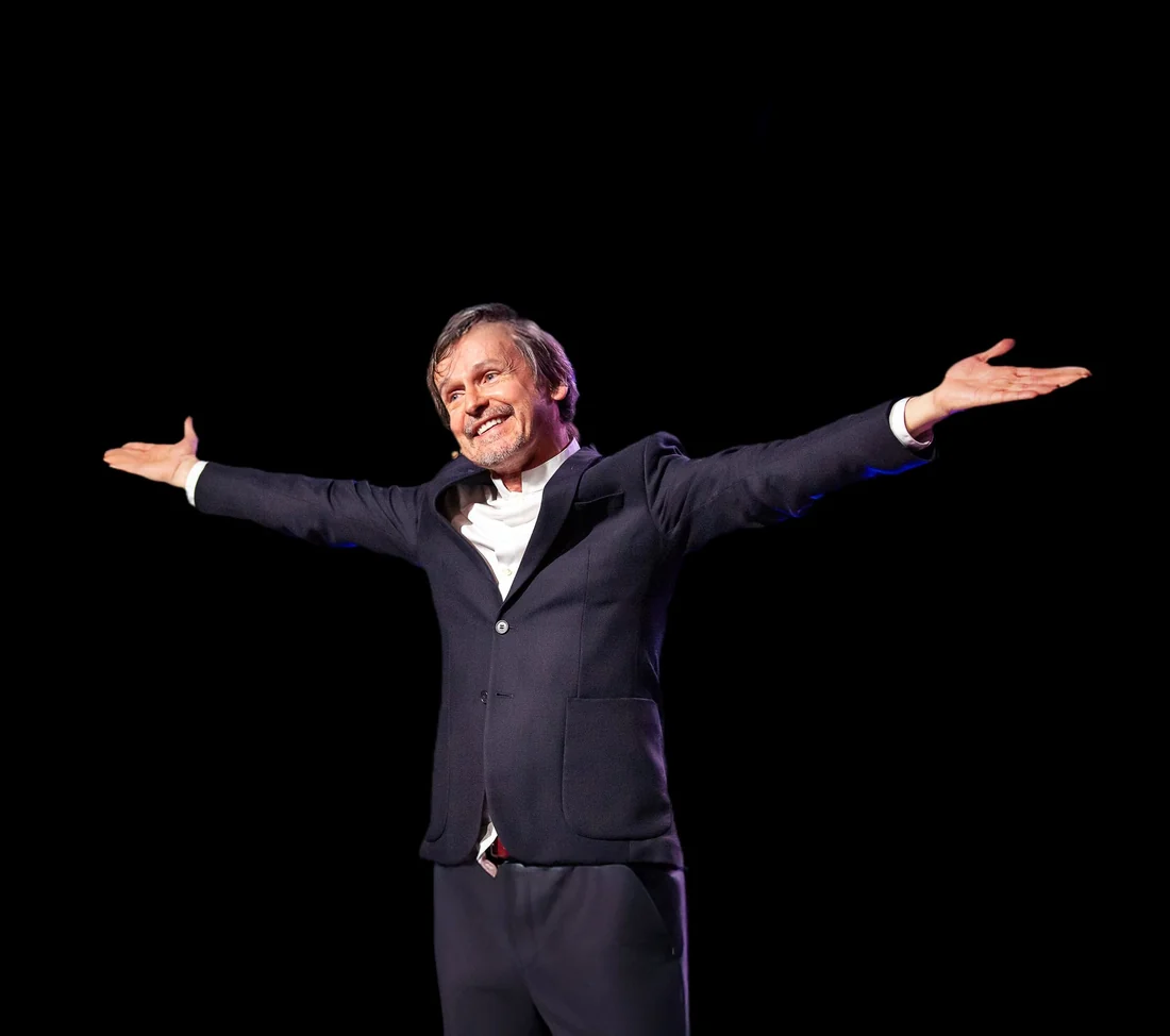 Dany Parmentier sur scène, bras ouverts, dans son one-man-show Gourou