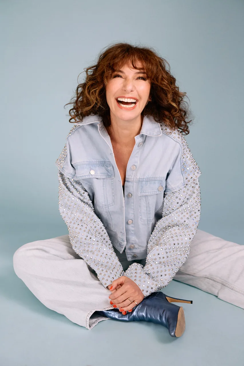 Anne Depetrini en tournée avec son spectacle À Côté, riant en veste en jean sur fond bleu